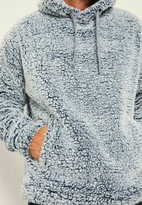 Himmelblauer, flauschiger Kapuzenpullover aus weichem Material mit strukturiertem Finish. Verfügt über eine Kapuze, Kordelzüge und Seitentaschen.