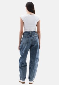 Bílé přiléhavé tričko, modré džíny s vysokým pasem a volným střihem, se zesvětlenými detaily, pěti kapsami a bílými teniskami s hnědou podrážkou.