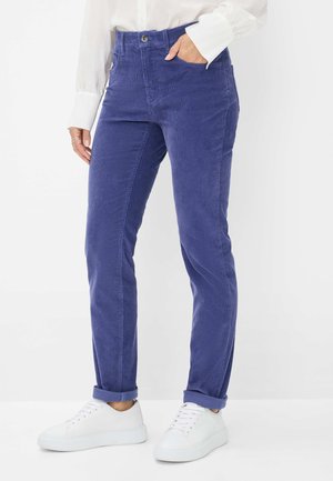 Lilla corduroy bukser med høj talje, med knaplukning, sidelommer og optrukne ærmer, parret med hvide sneakers.