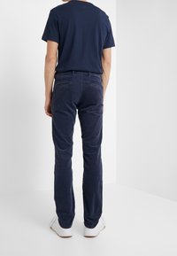 Laivastonsiniset corduroy-housut suoralla leikkauksella, joissa on kaksi takataskua. Yhdistetty yksiväriseen laivastonsiniseen T-paitaan ja valkoisiin tennareihin.