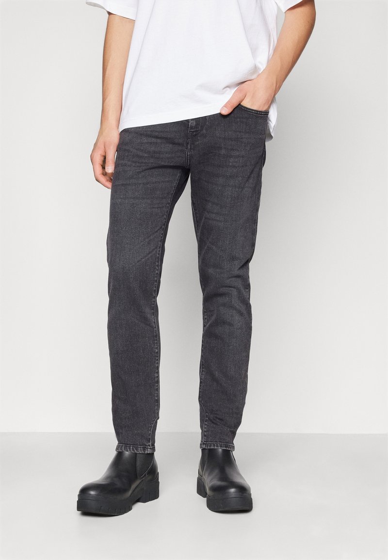 Jean en denim gris foncé à coupe slim, design cinq poches, avec une texture subtile, associé à des bottines noires.