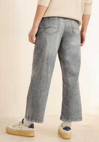 Pantalons larges en denim gris avec poches arrière et détails de coutures visibles. Associés à des baskets blanches et des chaussettes de cheville claires.