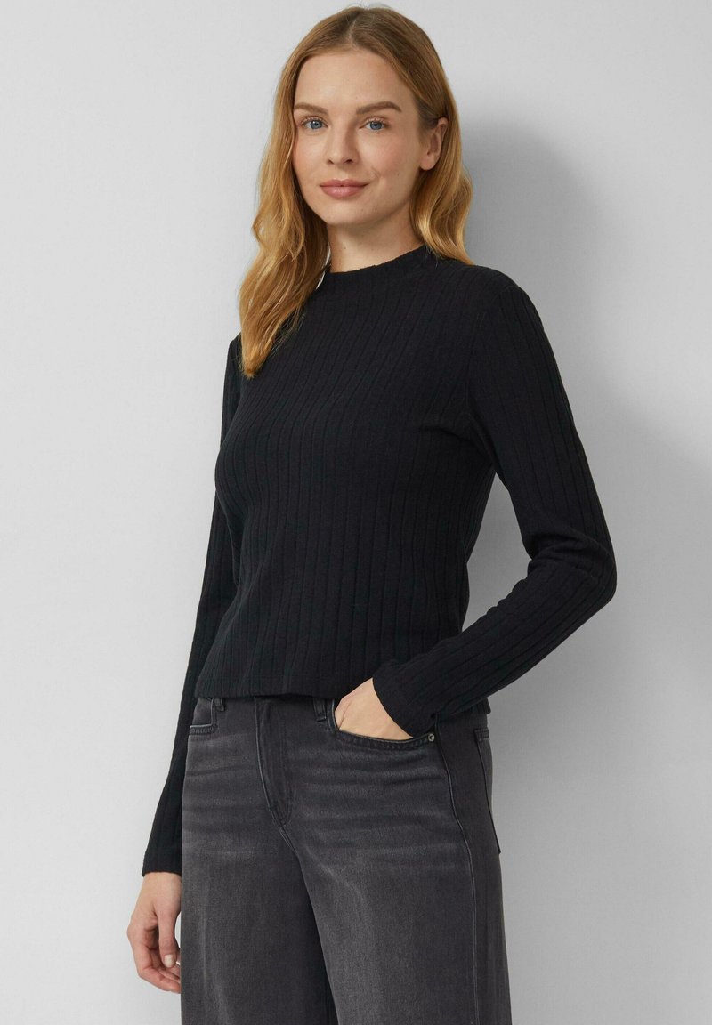 Czarny prążkowany top z długim rękawem, z wysokim dekoltem, dopasowany i o miękkiej fakturze, w zestawie z ciemnoszarymi spodniami dżinsowymi.