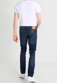 Mörkblå denimjeans med slim fit, med en läderlapp på baksidan av midjan och sydda bakfickor, matchat med en vit t-shirt.