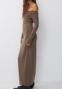 Vestido largo marrón ajustado con tejido acanalado, diseño off-the-shoulder y mangas largas, elaborado con una tela suave y texturizada.