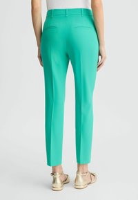 Turkusowe dopasowane spodnie o wysokim stanie wykonane z gładkiej tkaniny, z dwoma tylnymi kieszeniami. Noszone z złotymi balerinami.