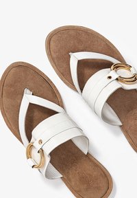 Bílé kožené sandály s překříženými pásky a zlatým kroužkem, s hnědou semišovou stélkou a plochou podrážkou.