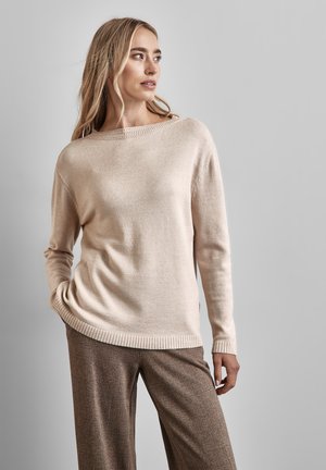 Beiger Strickpullover mit weitem Bootsausschnitt, gerippten Bündchen und Saum. Kombiniert mit strukturierten braunen weit geschnittenen Hosen. Glatte Stofftextur.