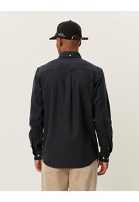 Chemise à carreaux foncée avec col structuré, manches longues et poignets ajustables. Dispose d'un pli dans le dos pour un meilleur ajustement.
