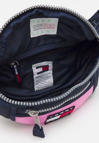 Pouch in tessuto blu navy e rosa con chiusura a zip argento. L'interno presenta etichette branding e una texture liscia e foderata. Design compatto.
