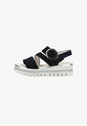 Black suede platform sandal with wide straps, large round buckle, and chunky white sole with deep treads.