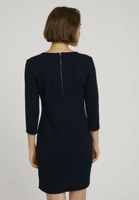 Marinblå strukturerad klänning med 3/4 ärmar, texturerad tyg och en synlig dragkedja bak. Figursydd siluett med knä-lång klipp.