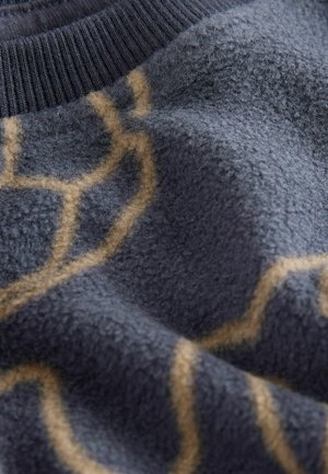 Blue fleece fabric with a soft, textured surface, featuring a tan geometric pattern. The edge has a ribbed knit collar.