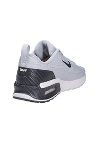 Grå atletisk sko med nätövre, svarta accenter, texturerad häl och synlig luftdämpning. Har en dragflik för enkel påtagning.