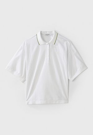 Hvitt polo-skjorte med korte ermer, med en knapp-stolpe, grønne og gule krage aksenter, samt sidestrikkede detaljer. LACOSTE-logoen er til stede.