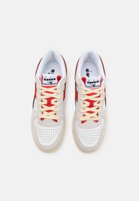 Hvite og grå sneakers med røde detaljer, kremfargede lisser og perforert tåboks; har en svart swoosh og polstret innside.