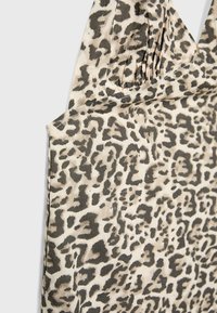 Tissu imprimé léopard avec des taches noires et beiges, avec des détails froncés près de la couture de l'épaule.