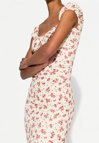 Kukka-aiheinen mekko, jossa on neliön muotoinen pääntie, lyhyet puffihihat ja ribbitekstuuri. Mekossa on kermavalkoinen tausta, jossa on punaisia ja vihreitä kukkakuvioita.