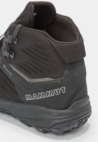 Bota de senderismo negra con parte superior sintética texturizada, que cuenta con un collar acolchado, etiqueta GORE-TEX y una distintiva suela de goma con tracción.