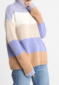 Pull en tricot avec un col haut présentant des rayures verticales en lavande, blanc cassé, beige et brun clair. Coupe ample et tissu texturé.