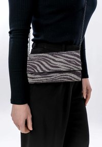 Metallist käekott, millel on musta ja hõbedase värviga siksakiline muster, mis sisaldab kettkübarat ja klapiga disaini.