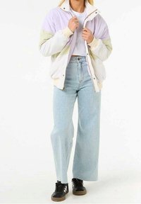 Licht gevoerde jas met pastelpaars en groene panelen, ritssluiting aan de voorkant, geribbelde manchetten. Gecombineerd met verwassen blauwe wijde broekjeans en zwarte sneakers.