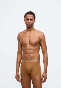 Brązowe bokserki wykonane z bawełny z miękkim pasem w talii, na którym znajduje się biały napis "TOMMY HILFIGER". Gładka faktura, dopasowany krój.