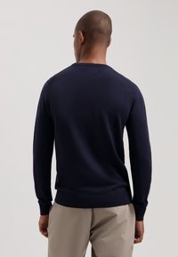 Navyblauer Langarmpullover mit Rundhalsausschnitt, weicher Textur und gerippten Akzenten an den Bündchen und dem Saum, kombiniert mit beigen Hosen.
