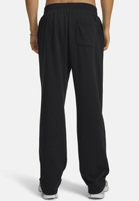 Zwarte joggingbroek met een elastische tailleband, losse pasvorm en een enkele opgestikte zak aan de achterkant. Gladde textuur en eenvoudig ontwerp.