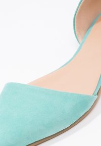 Aqua mockasins med spetsig tå och platt sula. Överdelen har en djup V-skärning som visar en mjuk innersula.