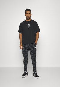 T-shirt en coton noir avec logo et étoiles, associé à un pantalon noir à motifs avec des rayures blanches et logo. Terminé avec des baskets noires.