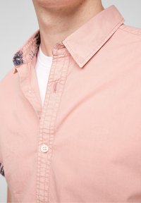 Růžová košile s krátkými rukávy, kontrastním vzorovaným límečkem, zapínáním na knoflíky a textura látky s viditelnými švy.