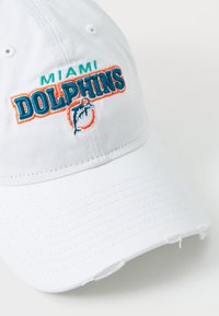 White baseball cap featuring embroidered "Miami Dolphins" logo in teal and orange, with a distressed brim and textured fabric.