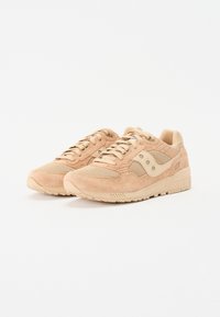 Beige suède tenisice s mrežastim akcentima, okruglim vrhom, ravnim vezicama i teksturiranim gumenim đonom. Sadrži logo na bočnoj strani i podstavljeni ovratnik.