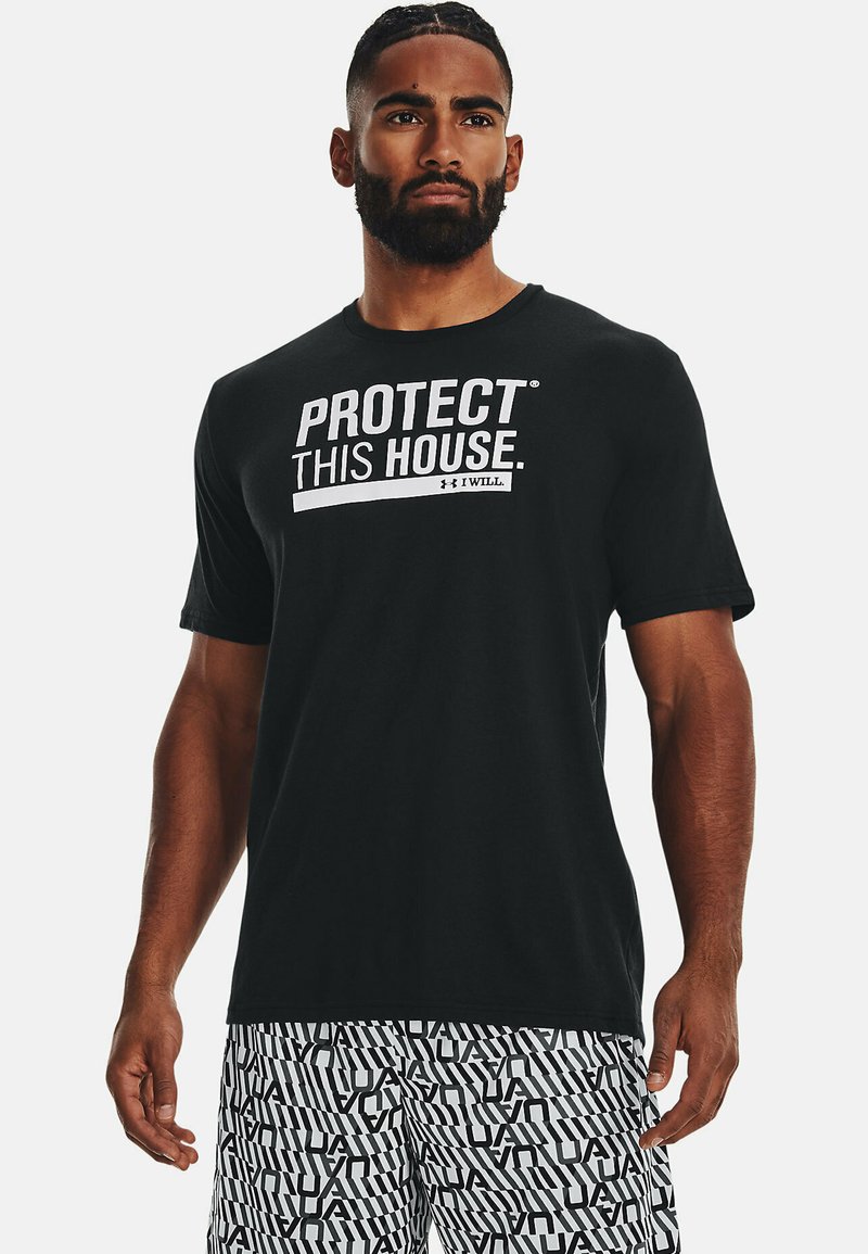 T-shirt noir avec le texte "PROTÉGEZ CETTE MAISON" en blanc. Manches courtes, col rond. Associé à un short à motifs noir et blanc.