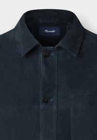 Marineblauwe suède jas met een klassieke kraag, twee knopen en een borstzak. Gladde textuur met blauwe stikselaccenten.