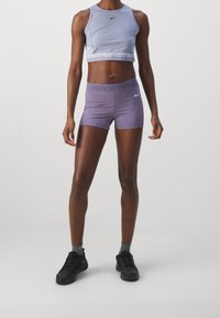Vaaleanlila urheilullinen crop top, jossa on pyöreä kaula-aukko, yhdistettynä samaan sävyyn korkeavyötäröisiin shortseihin. Molemmissa on valkoinen Nike-logo.