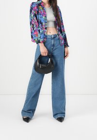 Veste à motif floral en bleu, rose et vert, haut gris court, jean large bleu et sac à main texturé noir. Escarpins noirs pointus.