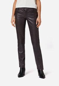Bruna läderbyxor i mörkt, med slim fit, framfickor och subtil glans. Kombinerat med svarta klackstövlar.