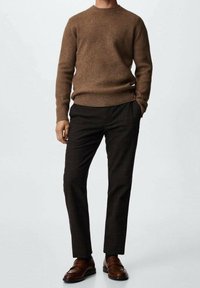 Maglione marrone a costine con scollatura rotonda, abbinato a pantaloni a quadri scuri e scarpe slip-on marroni. Texture liscia e design aderente.