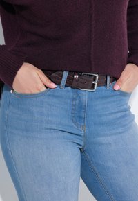 Mørk lilla strikket sweater parret med lyseblå tætsiddende jeans og et brunt bælte i krokodillemønster med en sølvspænde.