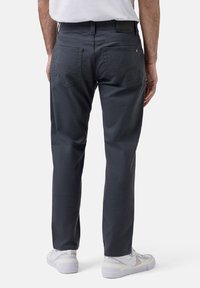 Pantalons en coton gris avec une coupe droite, dotés de deux poches arrière et d'une étiquette à la taille. Portés avec des baskets blanches.