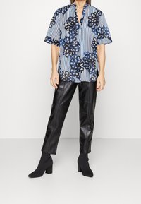 Blåstribet bluse med sort blomsterprint, korte ærmer og V-hals. Sammen med højtaljede sorte læderbukser og ankelstøvler.