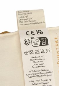 Puuvillane silt hooldusjuhistega: valge kude musta teksti ja sümbolitega, sisaldab CE ja UKCA märke. 100% orgaaniline puuvill.