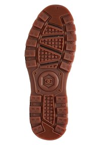 Brun gummisula av en sko med djupa spår och en cirkulär logotyp som har „DC“ och en stjärna i mitten.