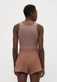 Débardeur marron à encolure arrondie associé à un short texturé de couleur marron clair. Le short a une taille élastique et une coupe décontractée.