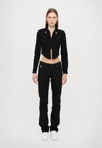 Black denim cropped jacket with gold accents, two chest pockets, and fitted sleeves, paired with black straight-leg jeans and white sneakers.