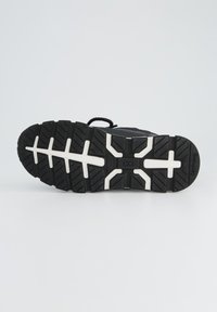 Semelle de chaussure de sport noire avec une surface en caoutchouc texturé, un motif de gomme bien marqué et des lignes d'accent blanches. Durable et conçue pour l'adhérence.