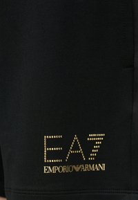Fekete rövidnadrág sima textúrával, bal oldalon arany strasszos "EA7 EMPORIO ARMANI" logóval és visszafogott dizájn részletekkel.