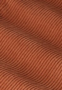 Tissu couleur rouille avec des crêtes ondulées surélevées et régulièrement espacées créant un motif texturé sur la surface.